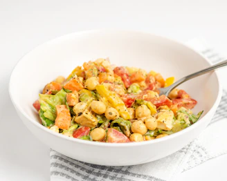 Colorful bowl of chickpea salad sprinkled with fresh herbs and lemon wedges on a rustic wooden table