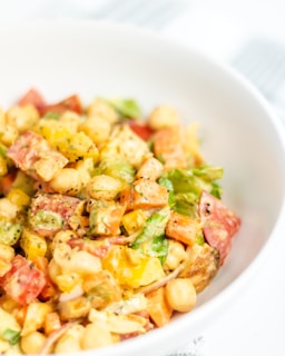 A colorful salad consisting of chopped vegetables such as bell peppers and lettuce, mixed with chickpeas and a creamy dressing. The ingredients appear fresh and vibrant, showcasing a variety of textures and colors.