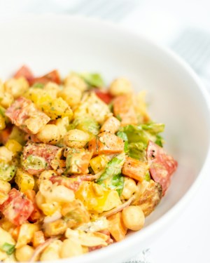 A colorful salad consisting of chopped vegetables such as bell peppers and lettuce, mixed with chickpeas and a creamy dressing. The ingredients appear fresh and vibrant, showcasing a variety of textures and colors.