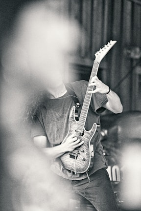 Close-up of a guitarist shredding on a black electric guitar with charcoal smoke in the background.