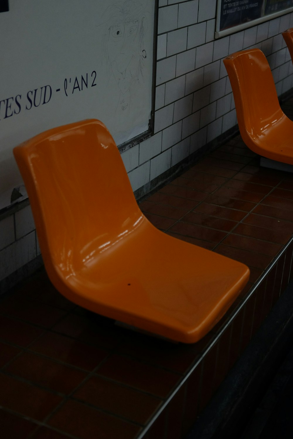 a row of orange chairs sitting on top of a tiled floor