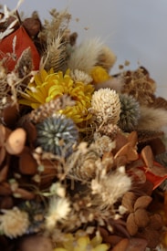 A composition of dried flowers and plants featuring various textures and colors. Prominent are yellow and orange elements, complemented by brown and beige shades. The diversity of shapes and sizes creates a rich, organic arrangement.