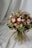A beautiful bouquet composed of a variety of flowers, including roses and daisies, with a mix of soft pink, deep red, and white blooms. The arrangement is lush, with green foliage and textured leaves, creating a vibrant and natural look. The backdrop features a draped white fabric that complements the colors of the bouquet.