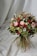 A beautiful bouquet composed of a variety of flowers, including roses and daisies, with a mix of soft pink, deep red, and white blooms. The arrangement is lush, with green foliage and textured leaves, creating a vibrant and natural look. The backdrop features a draped white fabric that complements the colors of the bouquet.