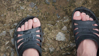 Close-up of sporty sandals with adjustable straps on a rocky trail.