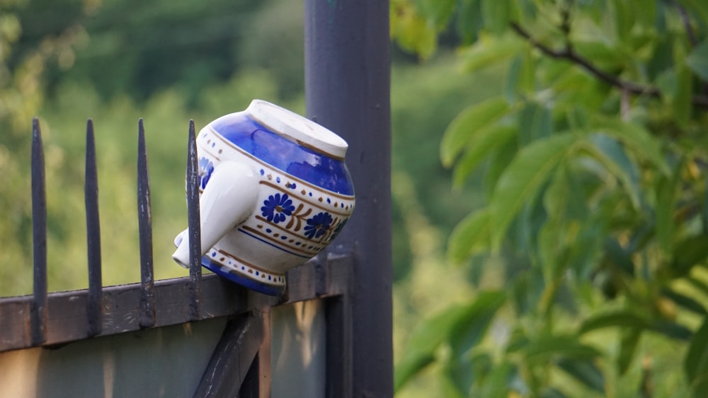 a blue and white vase sitting on top of a metal fence