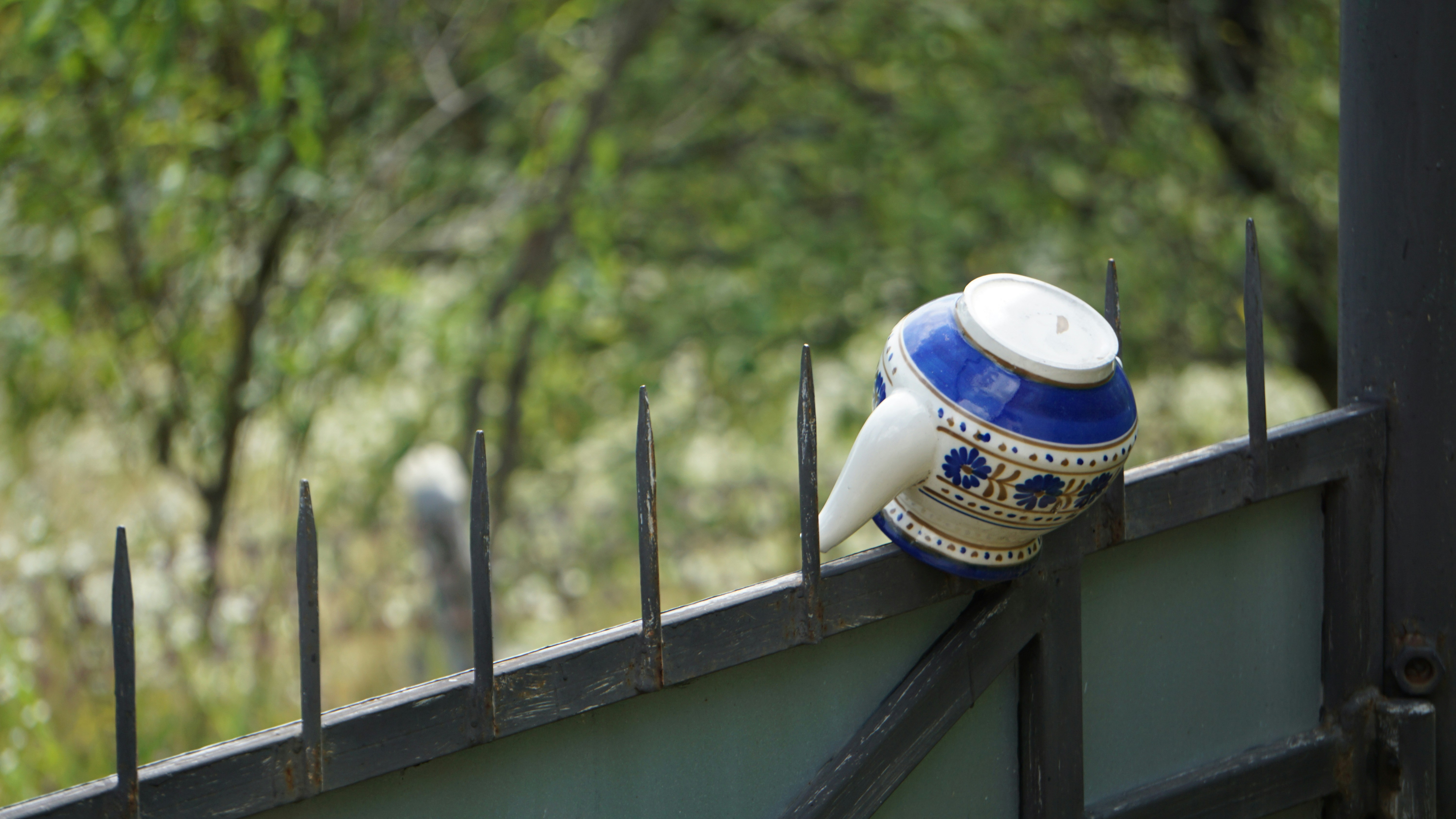 a blue and white tea pot sitting on top of a metal fence