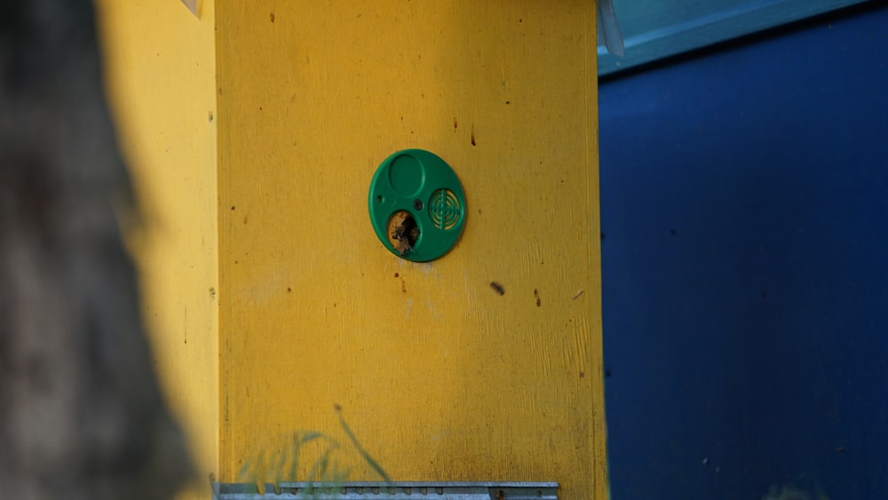 a green button on a yellow wall near a tree