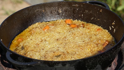 A large black pot contains a rice dish with visible pieces of cooked carrots. The rice appears to be seasoned and slightly oily, giving it a glistening sheen.