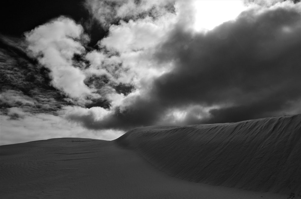 a black and white photo of clouds over a sand dune