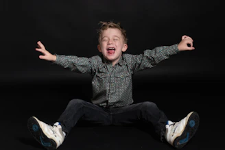 a young boy sitting on the ground with his arms wide open