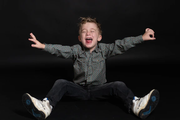 a young boy sitting on the ground with his arms wide open