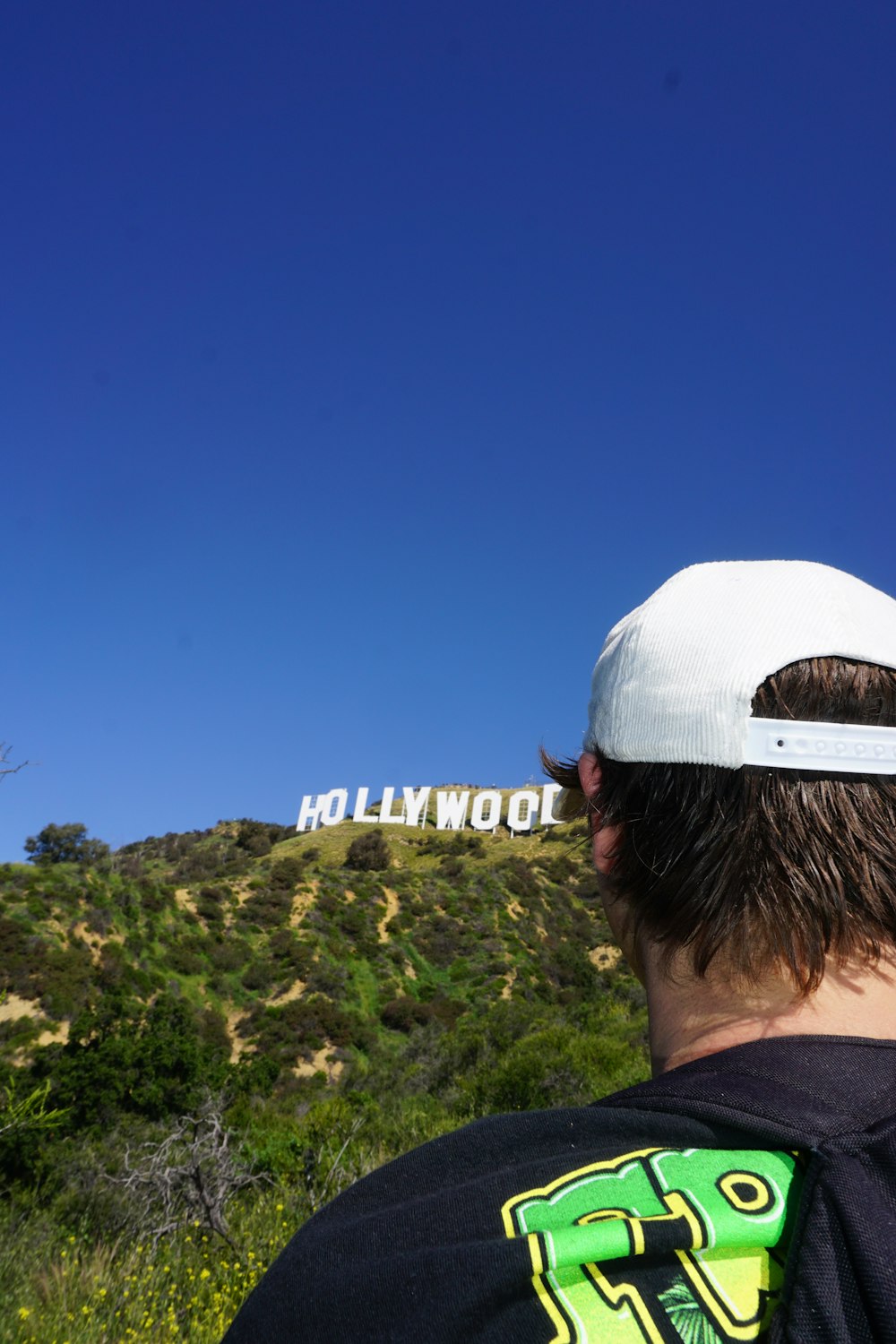 a man wearing a white hat looking at a hollywood sign