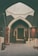 An arched interior space filled with a variety of colorful, patterned rugs displayed on the walls and laid out on the floor. Ceramic pots and other decorative items are showcased on a low table to the right, and framed artworks are stacked against the walls.