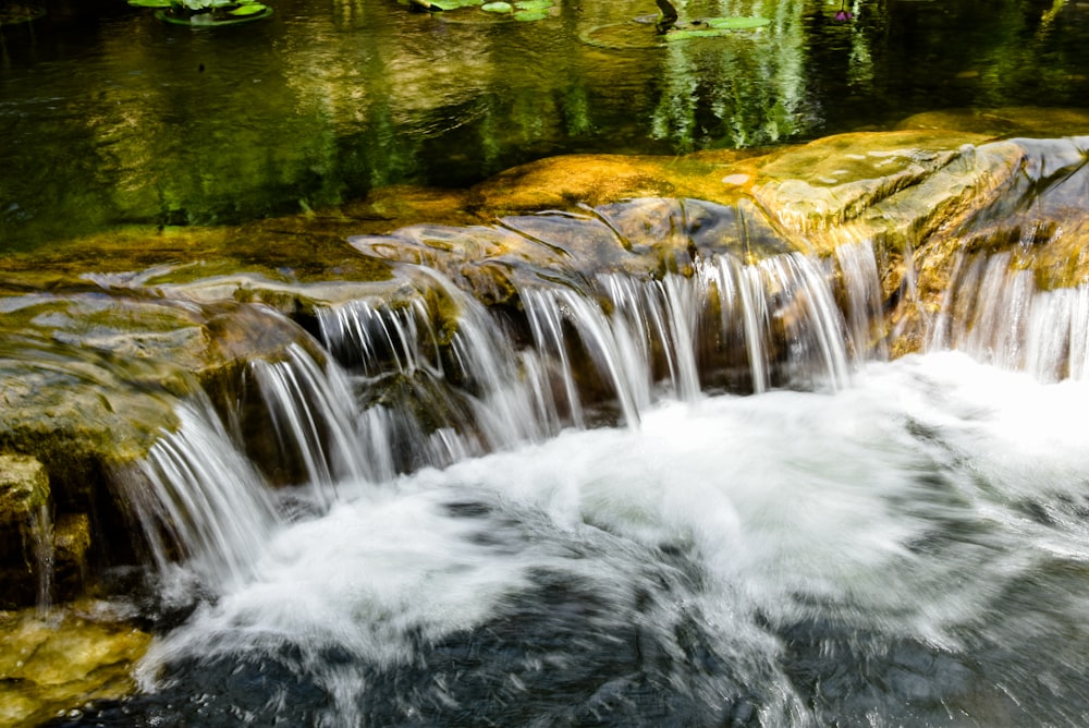 a stream of water running over rocks into a pond