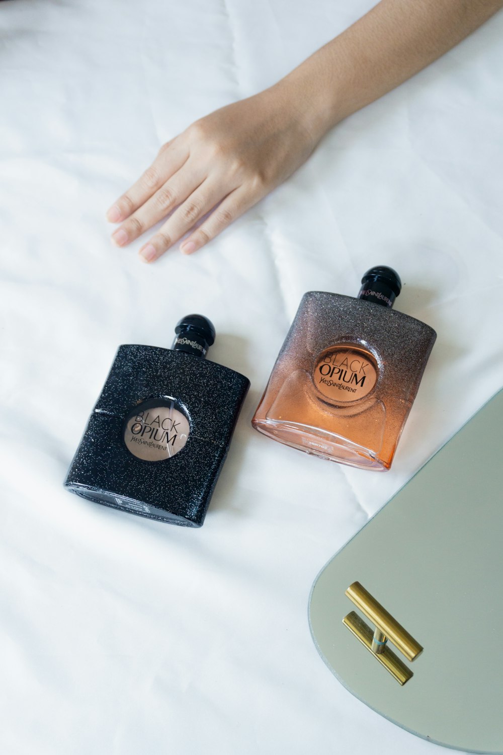 a person's hand on top of a bed next to two bottles of perfume