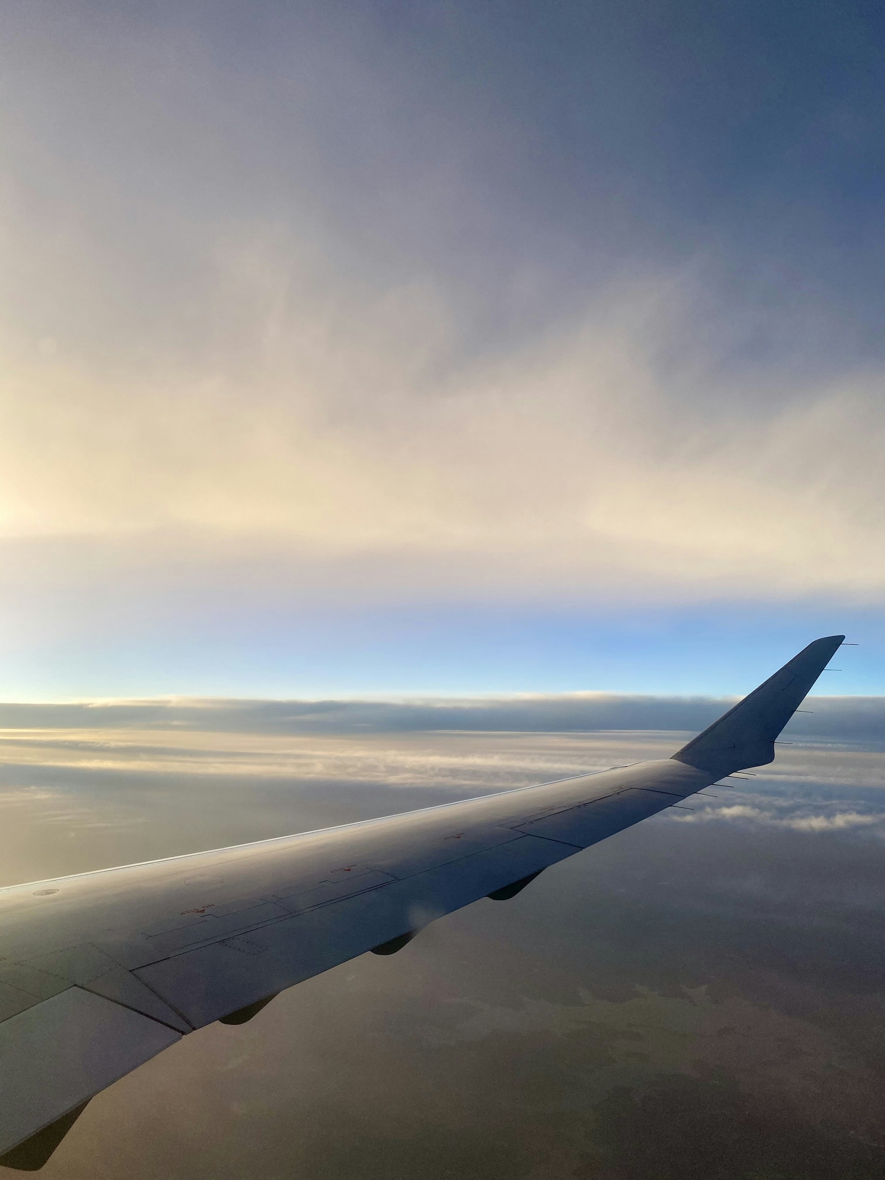 Airplane wing over clouds at sunset, golden hour sky, vast open blue atmosphere