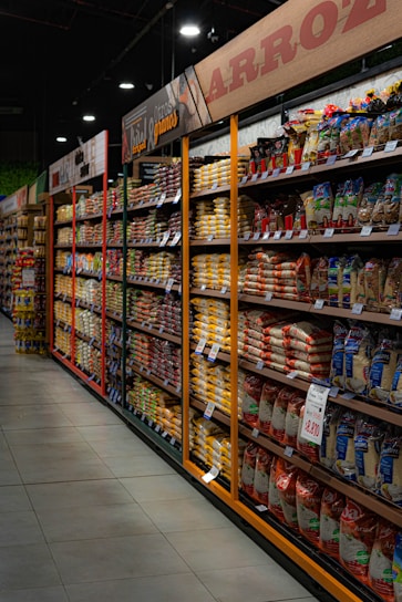 A bright, neatly organized aisle of rice and dal bags stacked on shelves in a wholesale grocery warehouse.