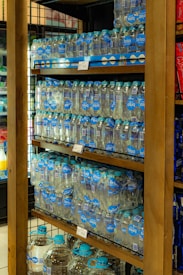 Shelves stocked with multiple packs of bottled water, organized neatly with clear labels displaying the brand 'brisa'. Each bottle has a blue cap and is part of a multi-pack held together by packaging. The shelves are wooden, and the setting appears to be in a retail environment with similar items displayed nearby.
