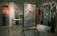 A dimly lit room features mannequins dressed in artistic clothing, showcasing a collection of garments with intricate patterns and vibrant colors. A decorative frame with frosted glass and bird and plant motifs stands in the center, surrounded by vibrant textiles and art pieces. The setting exudes an elegant and sophisticated atmosphere.