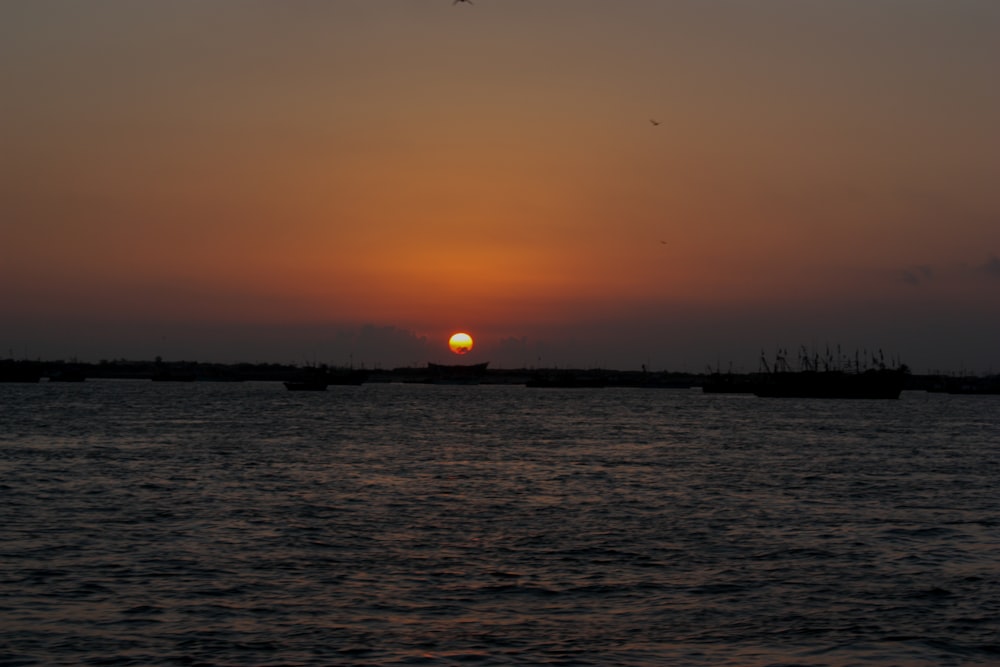 a sunset over a body of water with boats in the distance