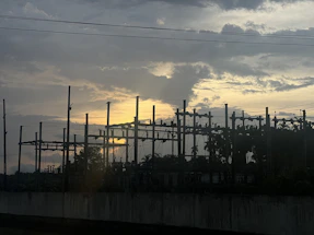A professional technician performing electrical testing on a substation transformer at sunset.