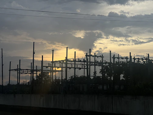 A professional technician performing electrical testing on a substation transformer at sunset.