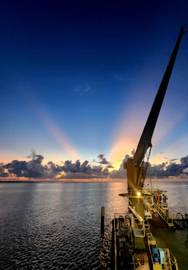 A certified crane operator guiding a heavy load with a 7-ton articulated crane at sunset on the Caribbean coast.