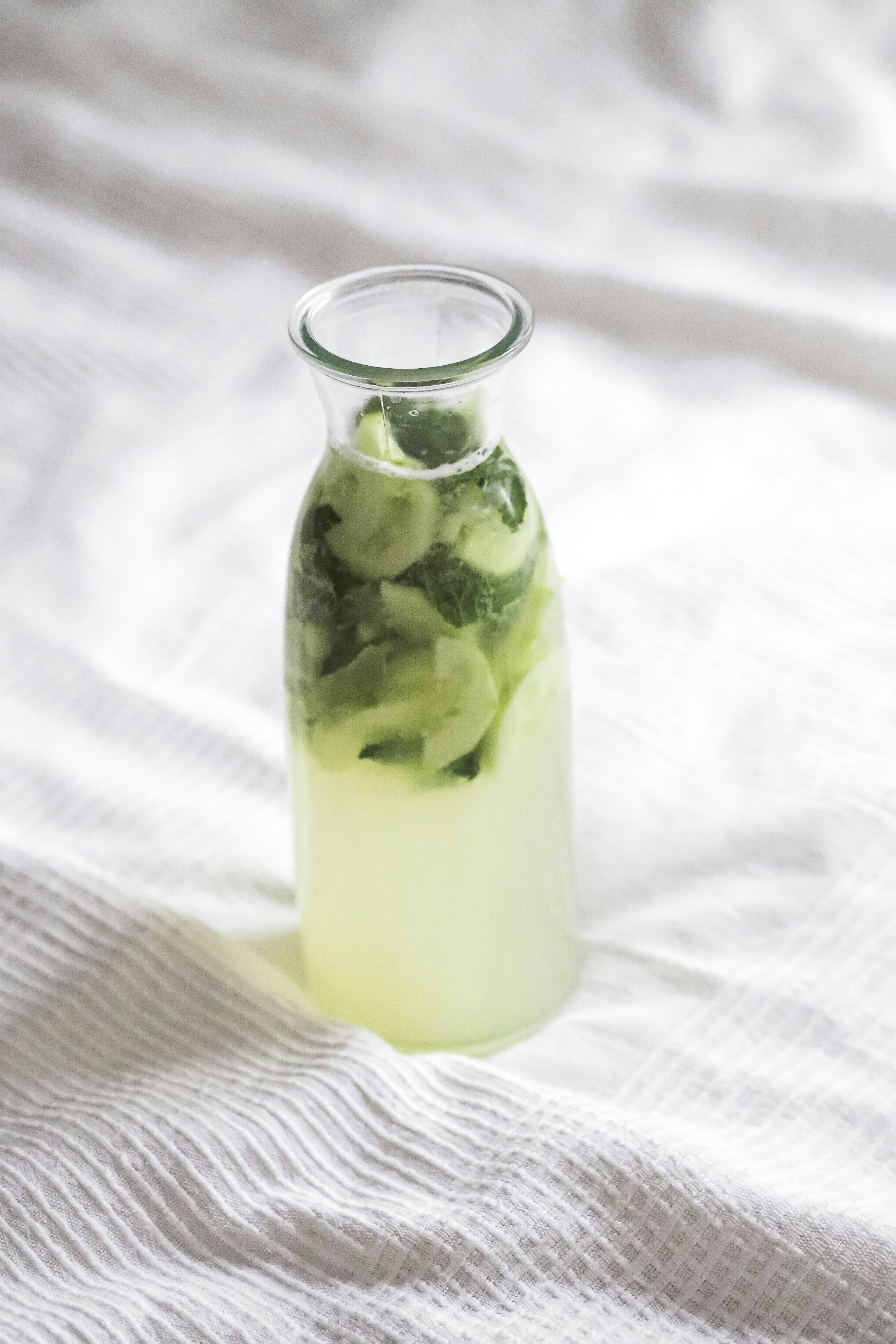 Tall glass bottle of cucumber mint infused water with cucumber slices and mint sprigs inside
