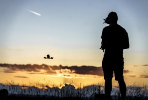 A sunset silhouette of a youth launching a small drone into the sky, symbolizing hope and future possibilities.