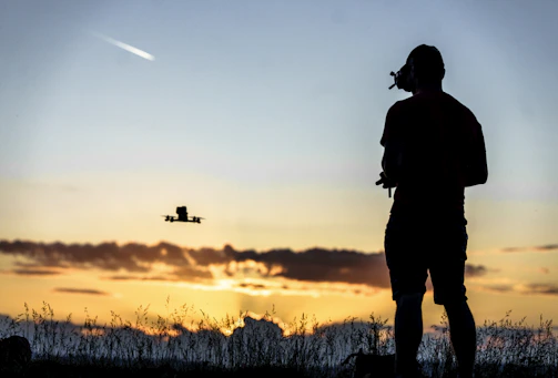 A professional surveyor using a drone over a construction site at sunset