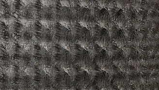 An intricate metallic mesh pattern with repeating, interconnected loops and curves, creating a visually dense and complex texture.