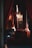 A dimly lit, opulent room with deep red velvet curtains and wooden paneling. A grand piano sits in the shadowy interior. The warm glow from multiple ornate light fixtures adds to the luxurious ambiance.