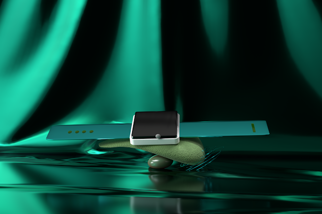 A modern smartwatch with a sleek black screen and turquoise strap is artfully balanced atop a smooth, textured stone. The background features a luxurious, shimmering green fabric, adding a glamorous aesthetic to the composition.