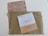 Three envelopes and a voting ballot are arranged on a flat surface. The largest envelope is brown with a text reading 'Elecciones Voto por Correo' and a stamp indicating it is urgent. On top of it, there are two smaller envelopes, one white labeled 'Diputados/as' and one beige labeled 'Senadores/as'. The voting ballot is partially visible beneath the envelopes, providing options for different political parties.