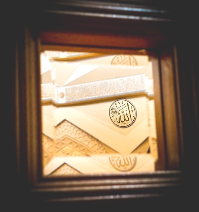 A detailed piece of Islamic geometric art featuring Arabic calligraphy. The artwork includes intricate patterns and a prominent circular motif with calligraphy in the center.