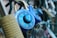 A close-up view of a blue combination padlock attached to a chain-link fence. The lock is prominently displayed in focus, with other padlocks blurred in the background. The numbers and the brand name on the lock are clearly visible.