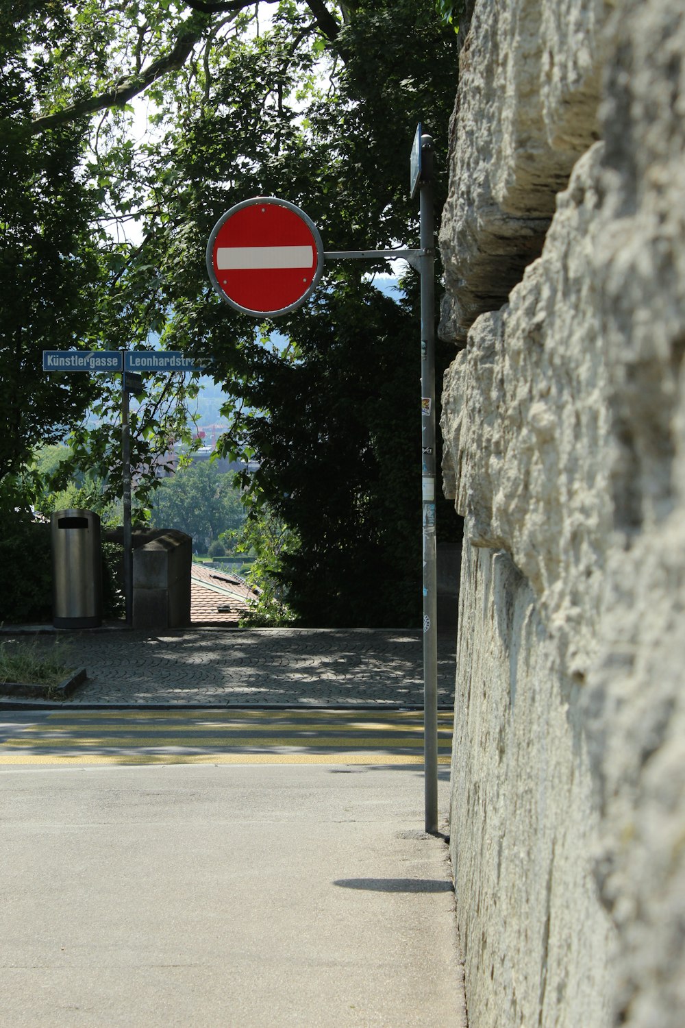 a red and white street sign next to a stone wall