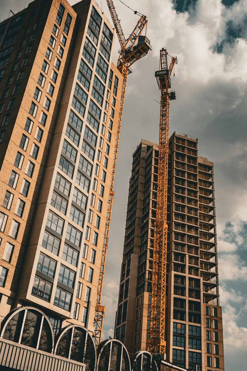 two tall buildings under a cloudy sky with a crane in the foreground