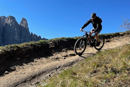 Mountain biker riding along a rugged trail with the Andes mountains towering in the background under clear blue skies.