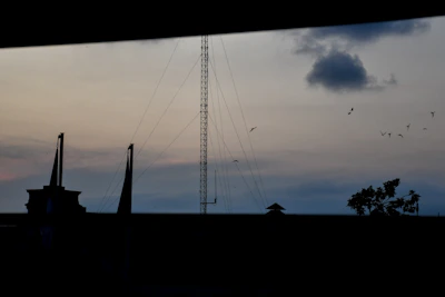 An outdoor shot of an antenna setup silhouetted against a twilight sky in Bangladesh, with faint radio waves illustrated around it.