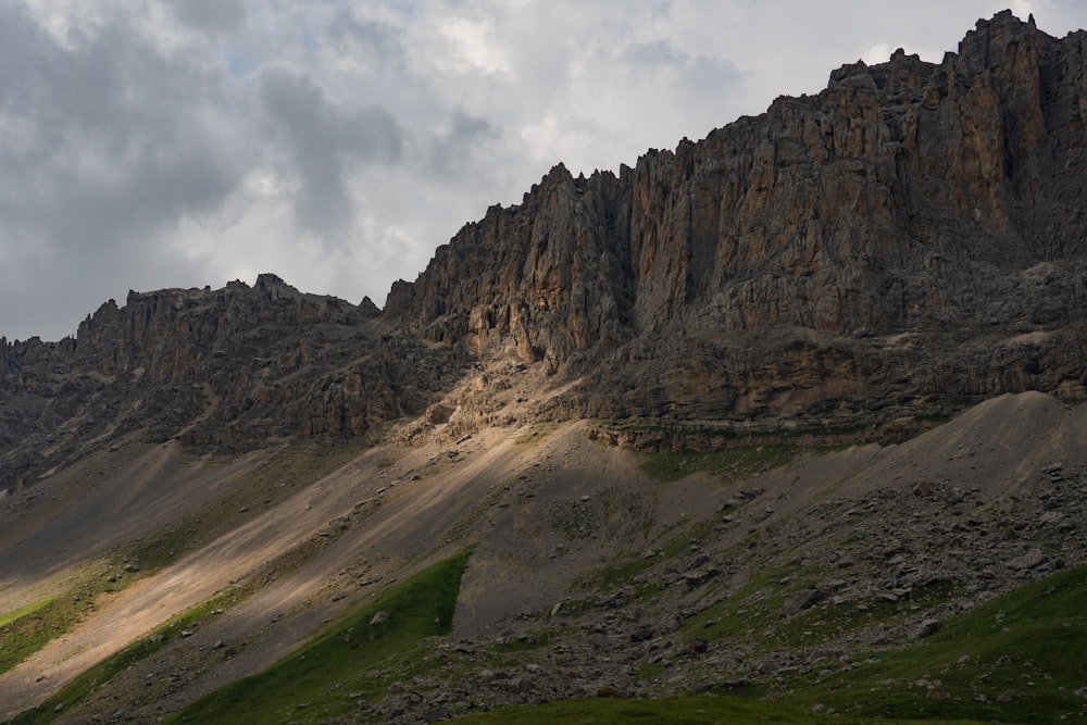 a rocky mountain with a green field below