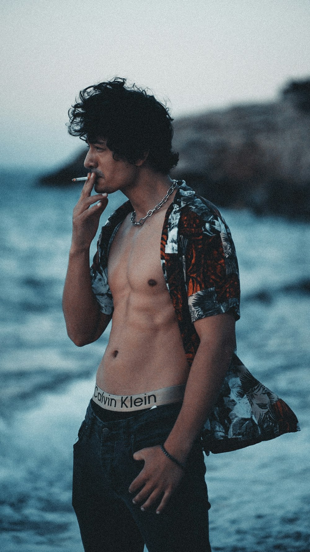 a shirtless man smoking a cigarette by the ocean