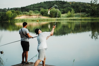 a couple of men standing on top of a pier next to a lake