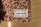 A close-up of a towel with a textured red and beige pattern is placed on a wooden surface. A label is sewn onto the towel, displaying the text 'Designed in Berlin Made in Germany towel.studio 100% Organic Cotton' along with care symbols.