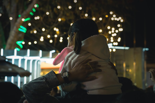 A vibrant street scene showing a mother carrying her toddler on her shoulders during a festival