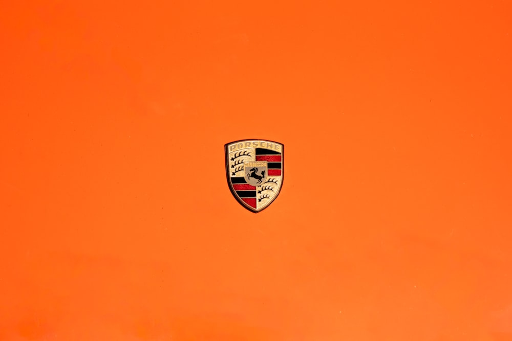 Un primer plano de un emblema de Porsche sobre un fondo naranja