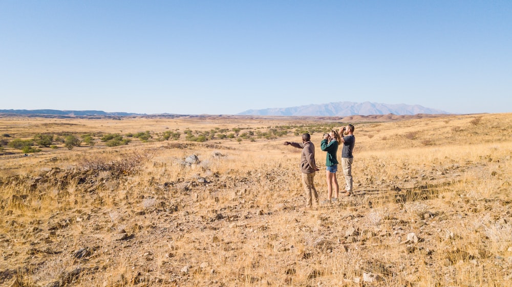 a group of people standing on top of a dry grass field