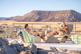 Guests relaxing on a sun-drenched deck, sipping drinks with a coastline in the background.