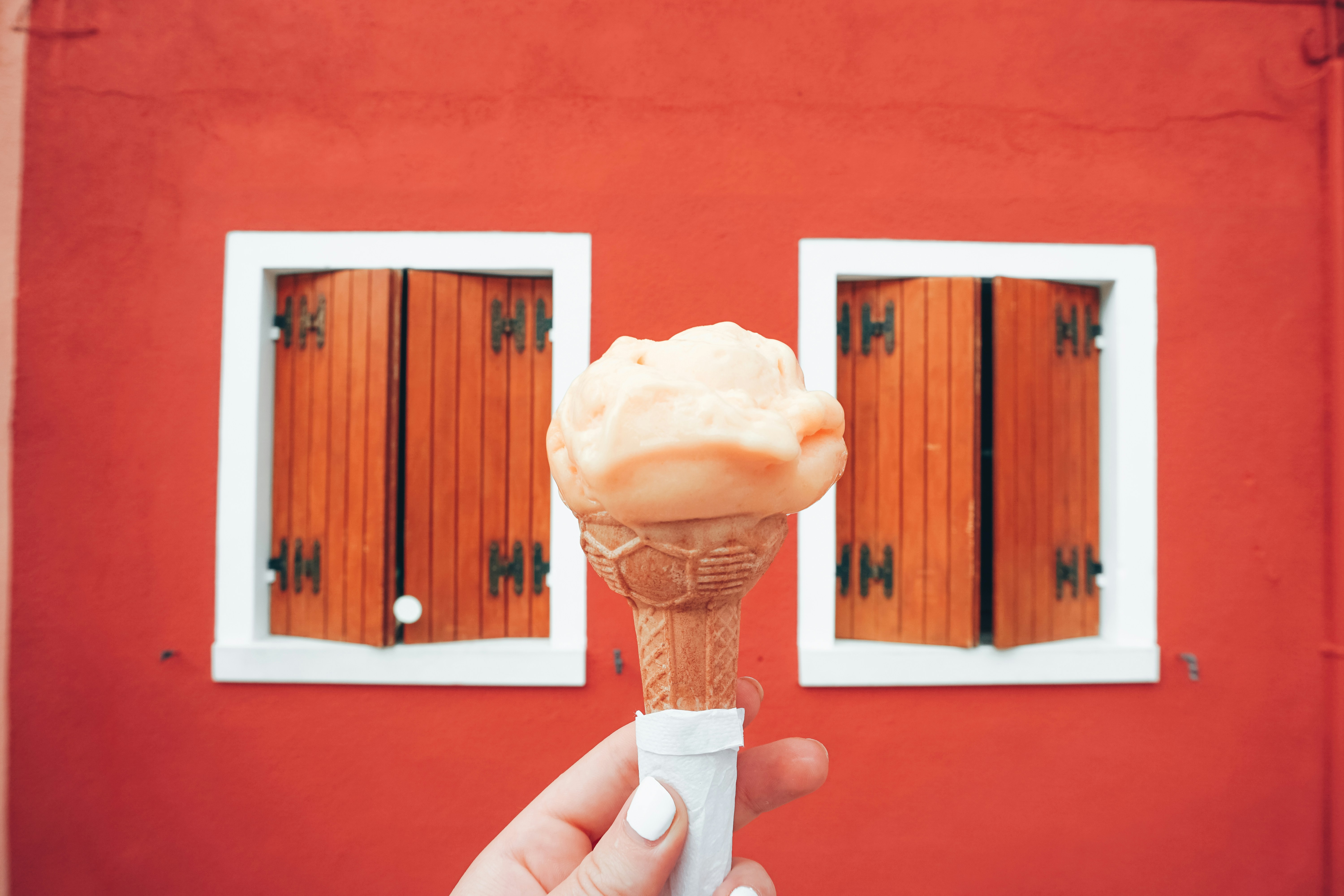 a hand holding an ice cream cone in front of a red building, gelato in italy